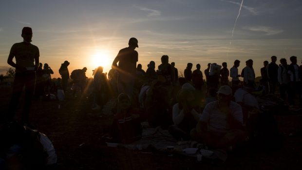Běženci při západu slunce stojí frontu na jídlo sběrném místě v obci Röszke