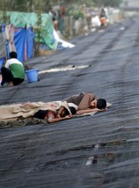 Indii sužuje vlna veder, muž odpočívá na plachtě vedle slumu