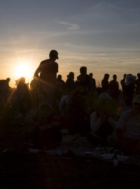 Běženci při západu slunce stojí frontu na jídlo sběrném místě v obci Röszke