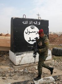 Irácký voják kráčí kolem zdi s namalovanou vlajkou Islámského státu (Mosul v lednu 2017)